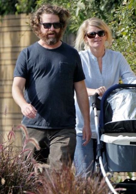 Quinn Lundberg in a white shirt poses a picture with husband Zach Galifianakis in a stroller.